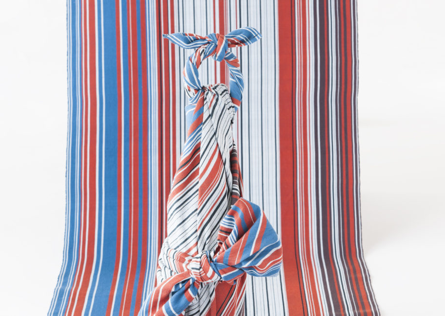 青赤黒白の細かいストライプの布と同じテキスタイルで作った風呂敷でボトルを包んでいる